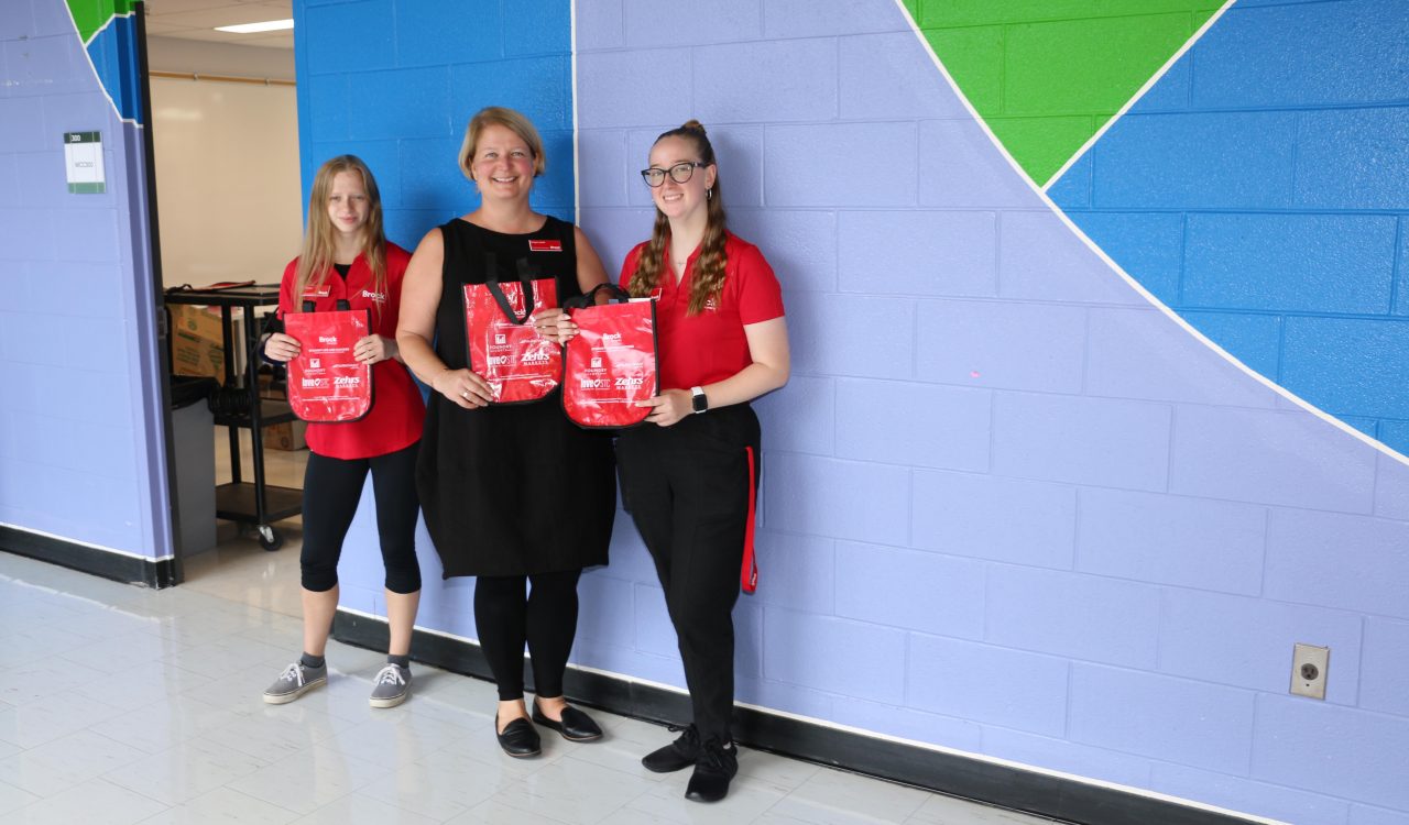 Three women hold red gift bags packed with print materials.