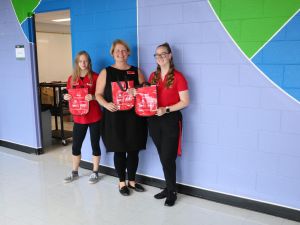 Three women hold red gift bags packed with print materials.