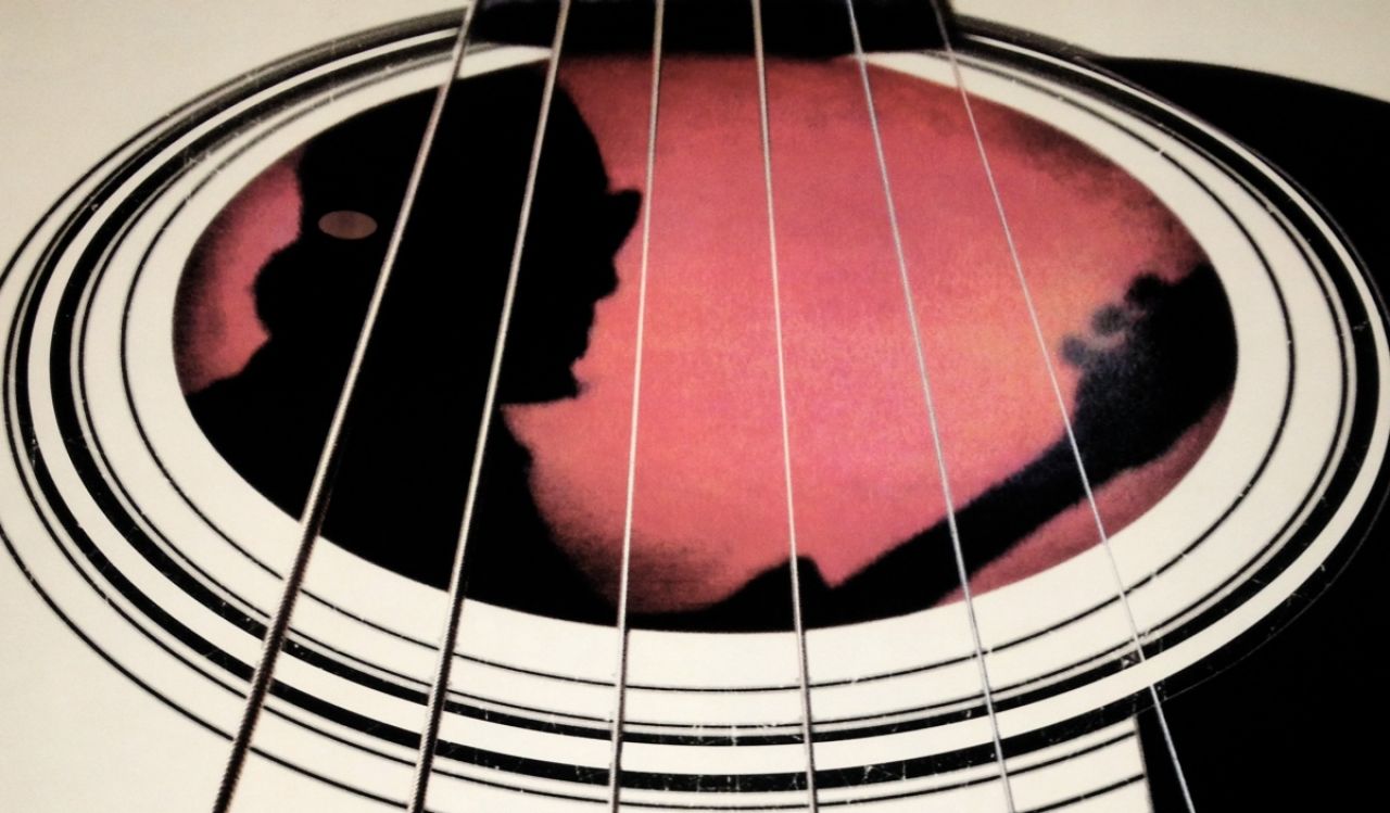 Movie poster for Searching for Sugar Man shows a black-and-white guitar with the silhouette Sixto Rodriguez holding a guitar backlit in pink.