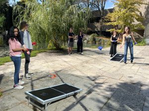 A group of university students enjoys a game of cornhole outdoors on a sunny day.
