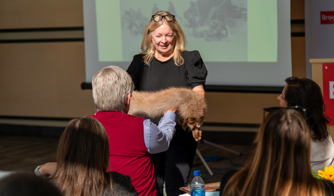 A woman, seen from behind, hands a fox pelt to another women during an presentation about Indigenous continuing education programs.