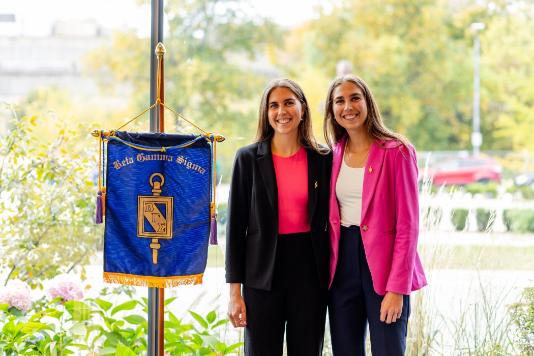 Alt Text: Two women stand with gold pins next to a hanging purple fabric banner.