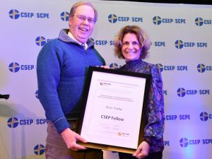 Peter Tiidus and Nota Klentrou hold a large framed “CSEP Fellow” award in front of a photo backdrop filled with a repeating Canadian Society for Exercise Physiology logo
