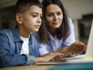 A boy uses a laptop with help from his mother.