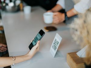 Woman's hand holding smartphone scanning a QR code for contactless payment in a coffee shop.