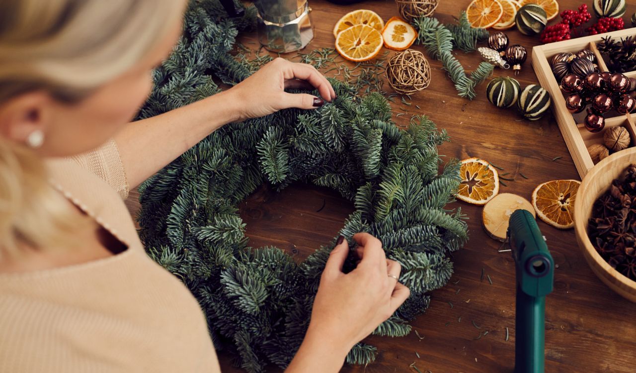 Close-up of unrecognizable woman standing at wooden table and using secateurs while cutting a fir twig for decorative evergreen wreath