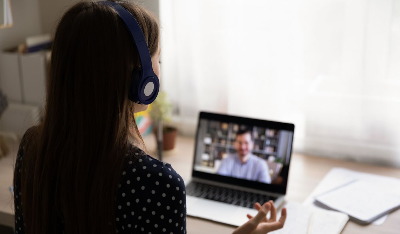 A woman looks at a laptop screen showing a video call.