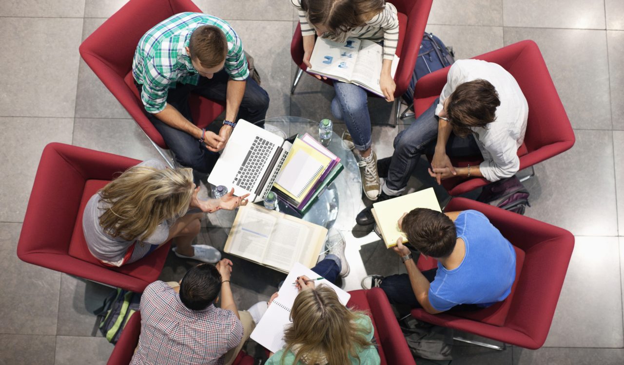 A group of people sit in a study circle with laptops and notepads.