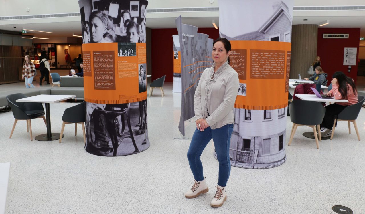 A woman stands in front of two pillars and a large wall display that have white text on an orange and grey background.