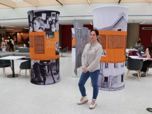 A woman stands in front of two pillars and a large wall display that have white text on an orange and grey background.