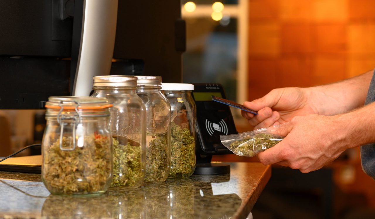 Hands paying by credit card for marijuana at a cannabis dispensary.