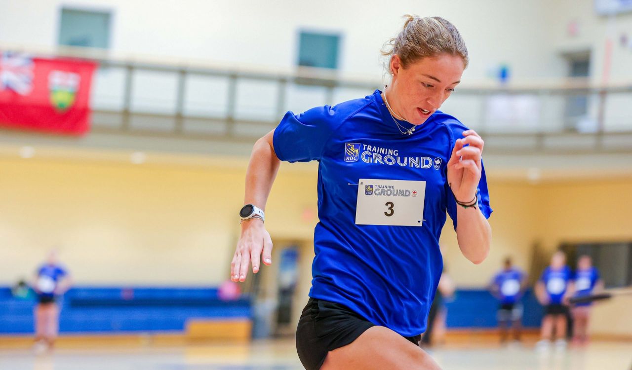 A woman wearing a blue T-shirt sprints inside of a gym.