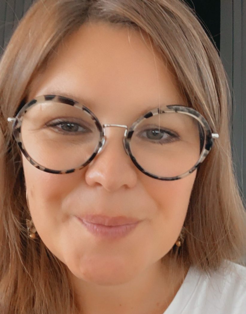 A woman in glasses and a white shirt takes a close-up selfie.