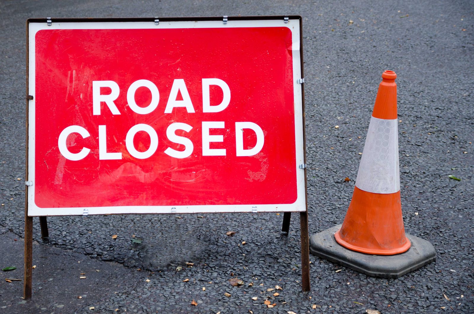 A sign saying ‘Road Closed in white letters on a red background next to an orange traffic cone.