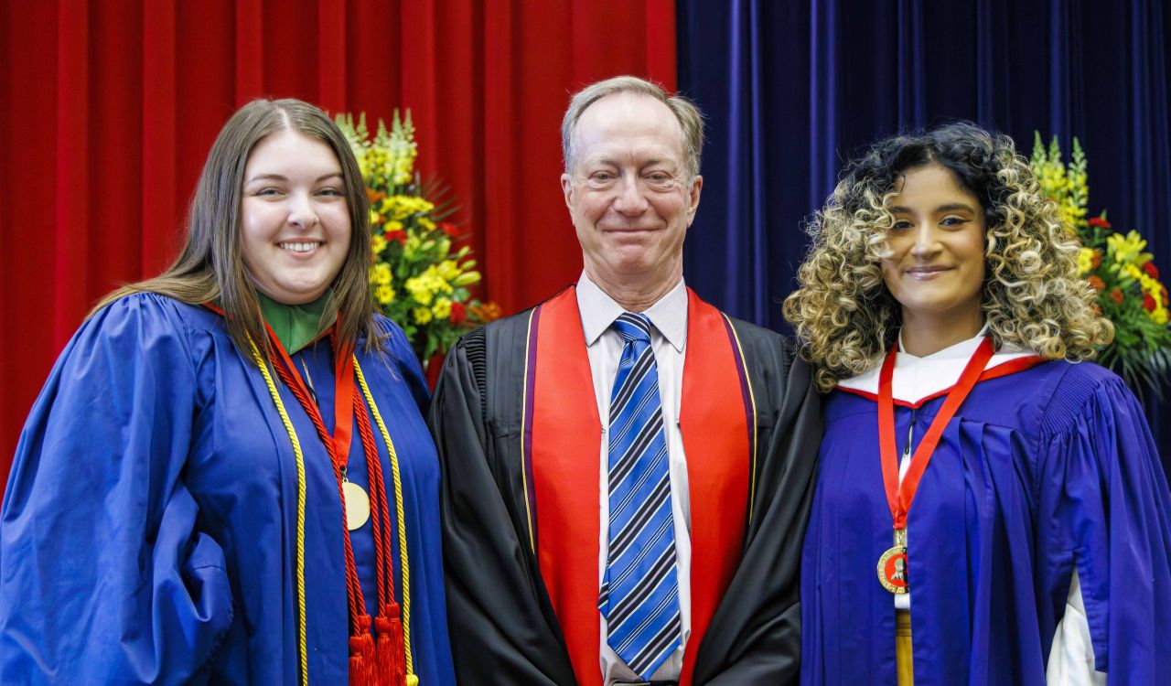 Three people in academic robes pose for a photo during a university graduation ceremony.