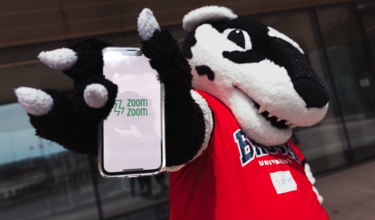 A badger mascot holds up a piece of paper with the words “zoom zoom” printed on it.