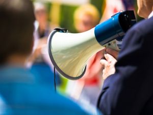 Man holding a megaphone while speaking to a crowd.