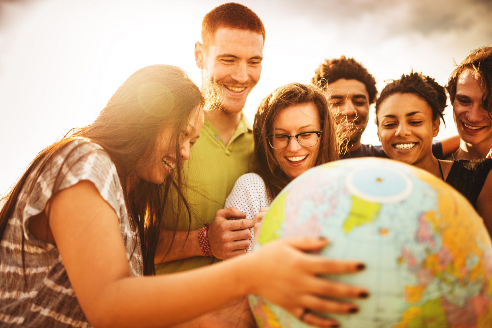 Smiling young adults hold a globe outside on a sunny day.