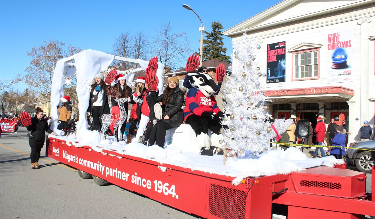 A red and white parade float holding a group of Brock University students and a mascot dressed as a badger.