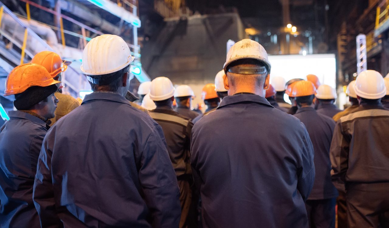 A group of workers in hardhats are seen from the back.