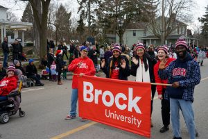 People walk in a parade holding a red Brock University banner.