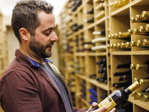 Brock employee Taylor MaGee examines the label of a bottle of wine in a wine cellar.