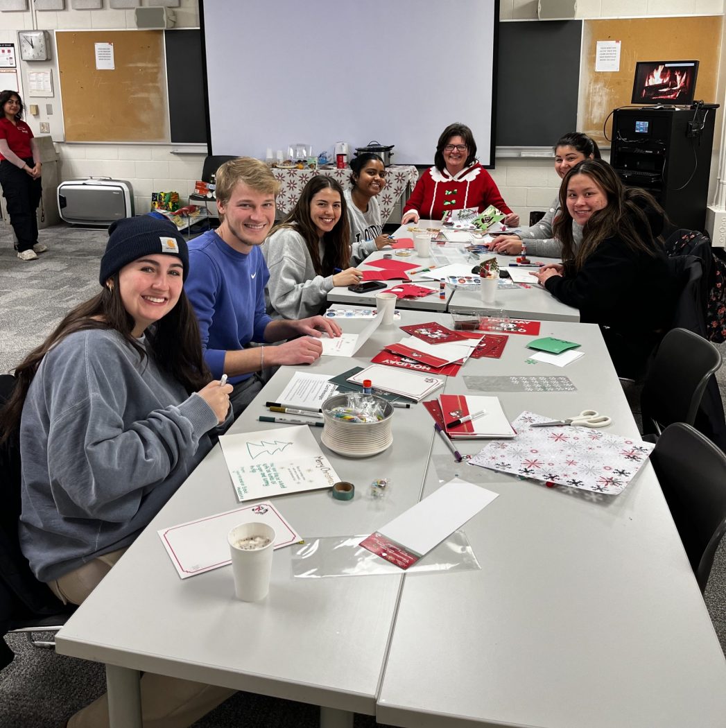 University students sit around a table making holiday cards for seniors.