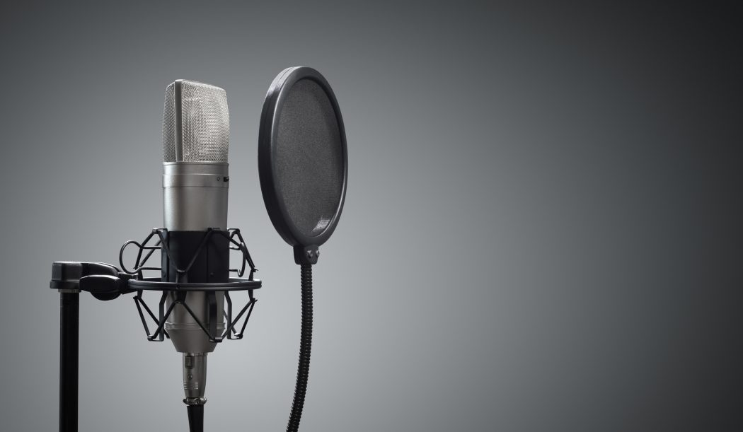 A black microphone sits in the centre of the frame against a grey background.
