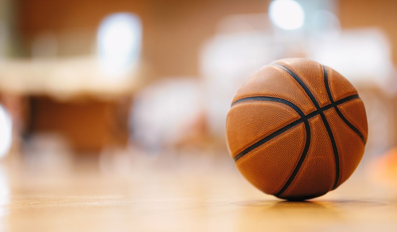 Close-up image of an orange basketball on a wooden gymnasium floor.