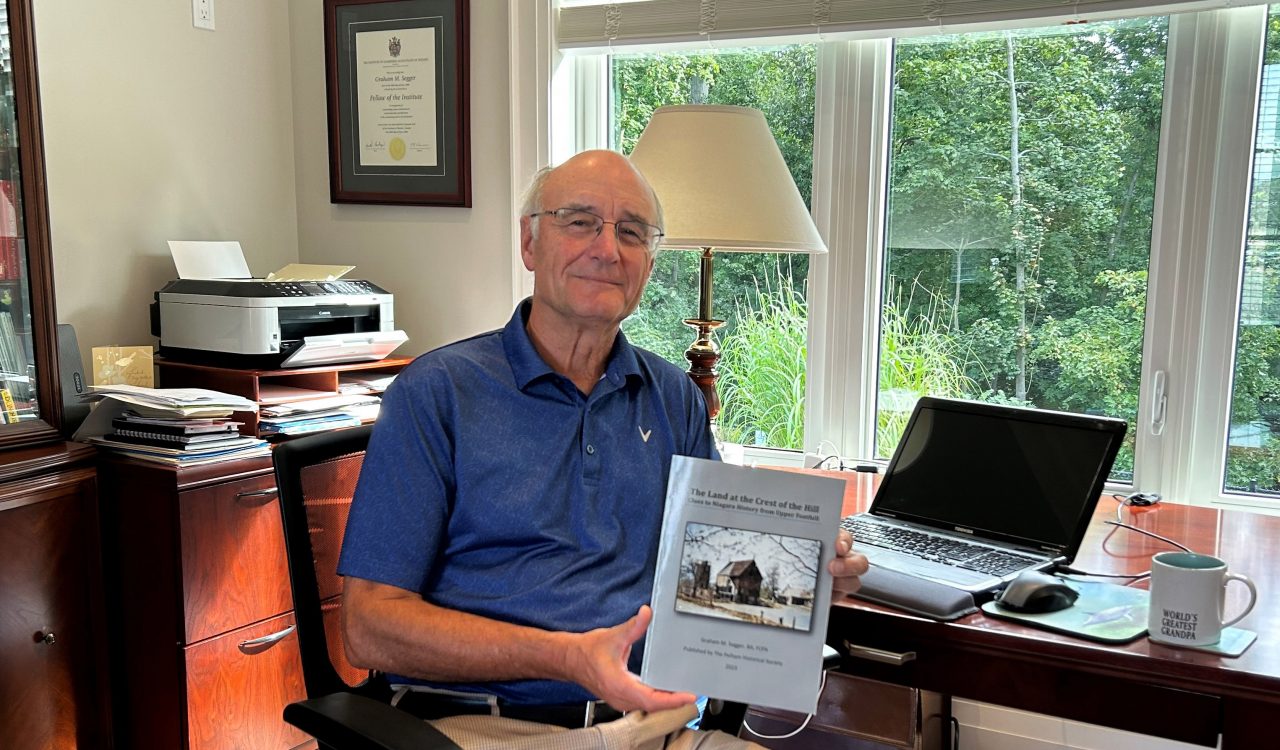 Graham Segger sits in his home office holding a published copy of his new book.