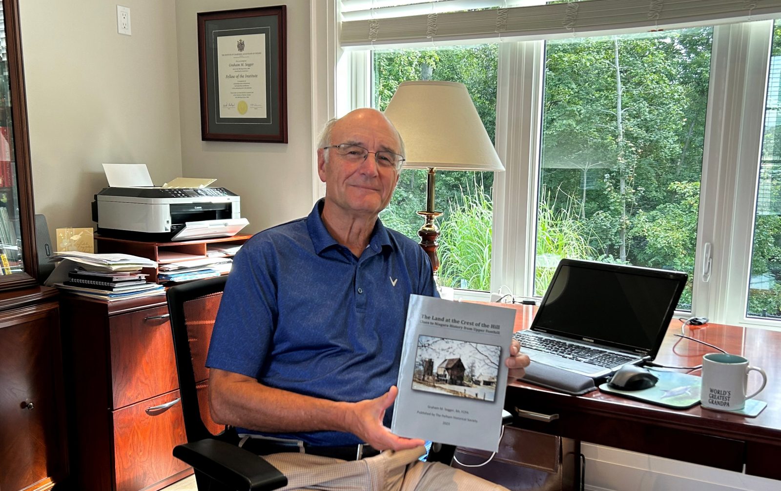 Graham Segger sits in his home office holding a published copy of his new book.