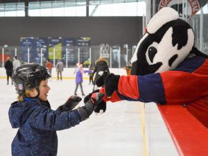 A child interacts with a badger mascot during a skating session.