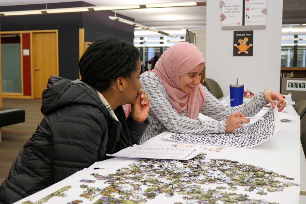 Two university students complete a crossword puzzle in a library.