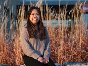 A portrait of Brock graduate student Mandisa Lau sitting outside in front of tall autumn grasses.