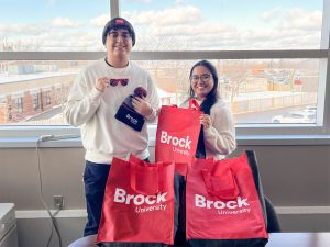 Two university students smile while holding Brock University promotional items.