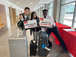 Three international students pose for a photo with their luggage.
