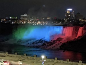 The American Falls at Niagara Falls illuminated in teal, blue and orange.