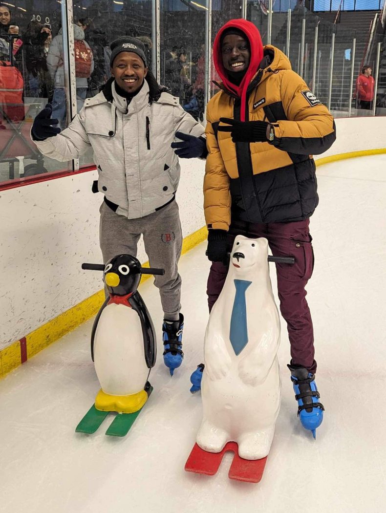 Two young men pose for a photo on an ice rink.