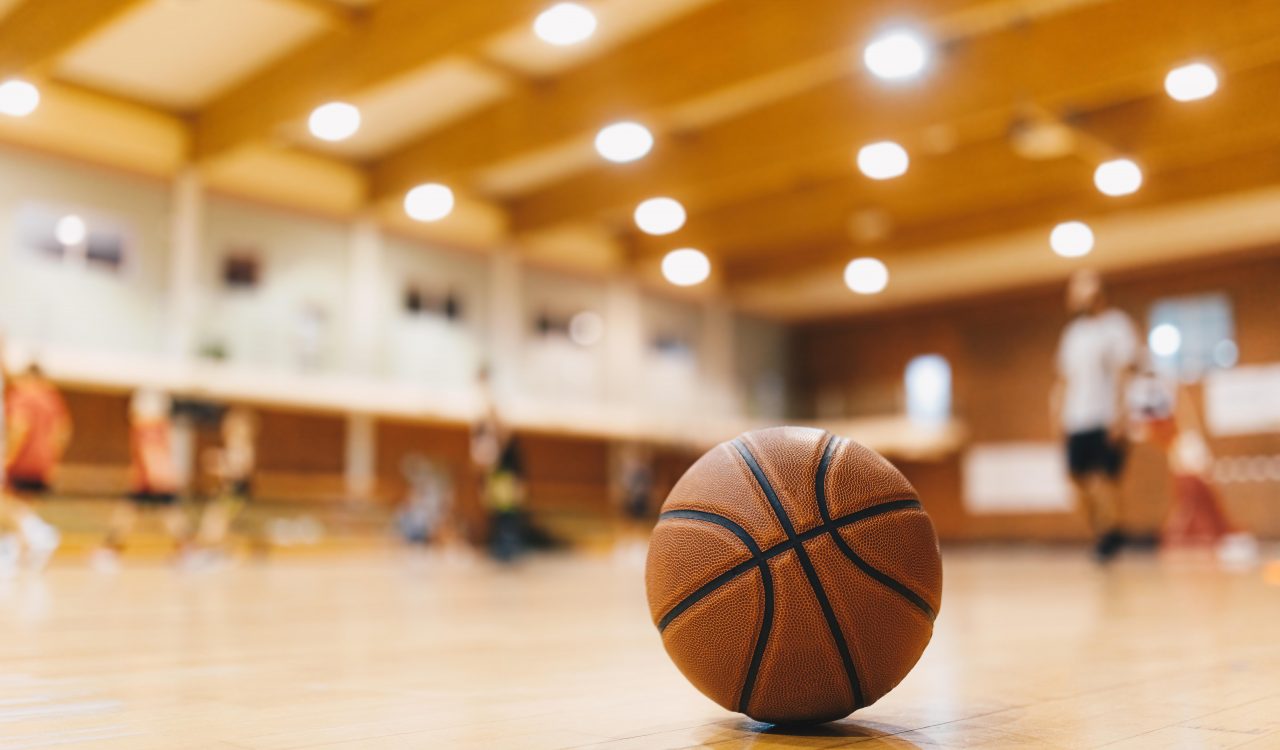 Basketball on Wooden Court Floor Close Up with Blurred Players Playing Basketball Game in the Background
