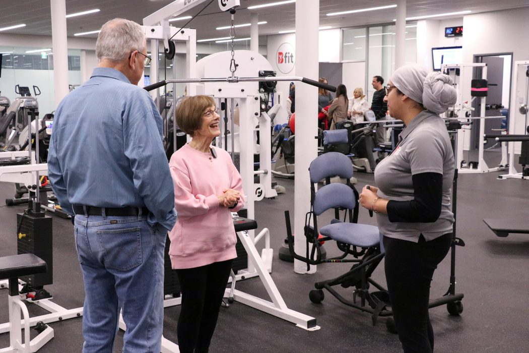 Two older adults converse with a staff person in a bright and spacious exercise facility.