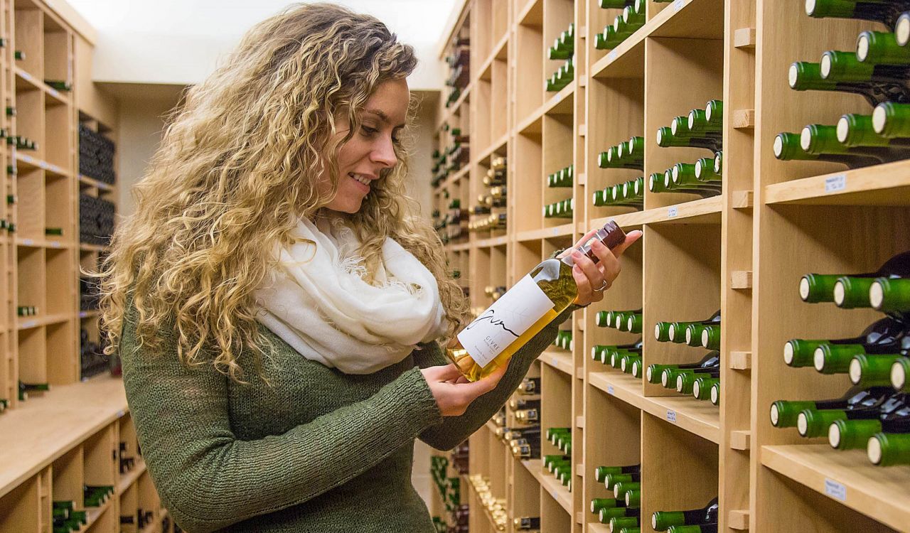 A woman inspects a bottle of wine while standing a wine cellar.