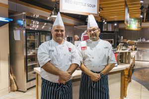 Two chefs in uniforms stand in a cafeteria.