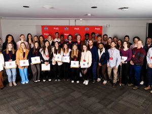 A group of student-athletes stand holding their academic awards in front of a Brock University-branded backdrop.