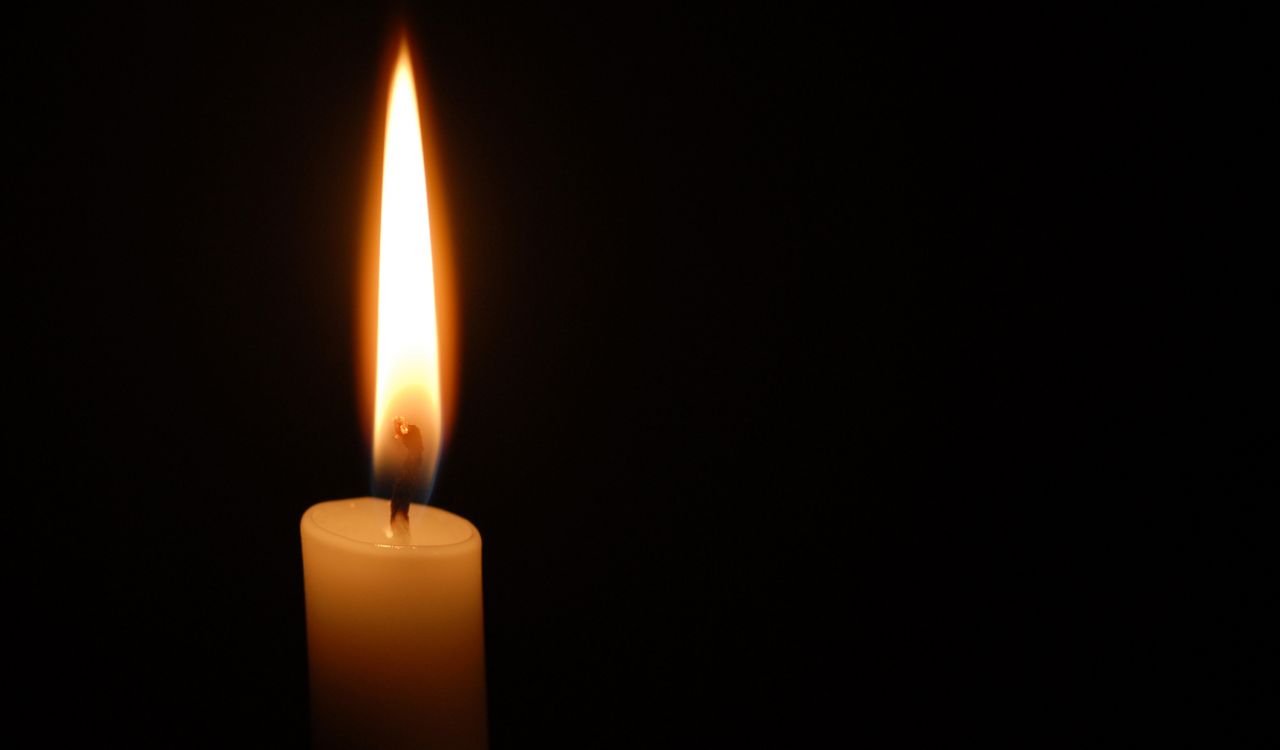 A lit candle burns against a black background.