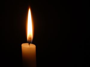 A lit candle burns against a black background.