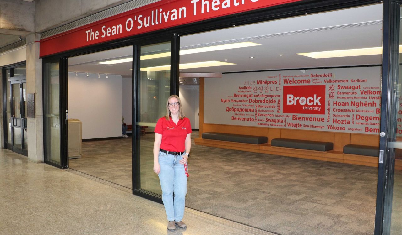 A woman wearing a red shirt stands below a sign that says Sean O’Sullivan Theatre