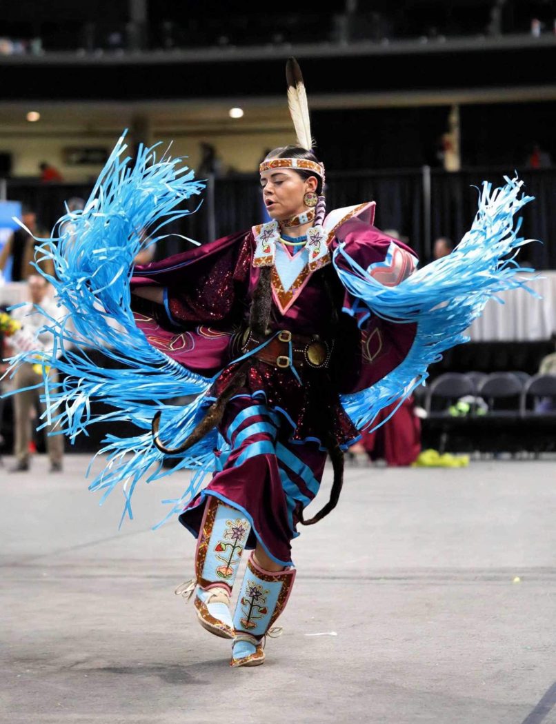 A woman wearing regalia dances at a pow wow.