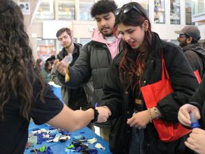 A female student stands in front of a male student as the pair makes stress balls. A third male student is in the background waiting in line.
