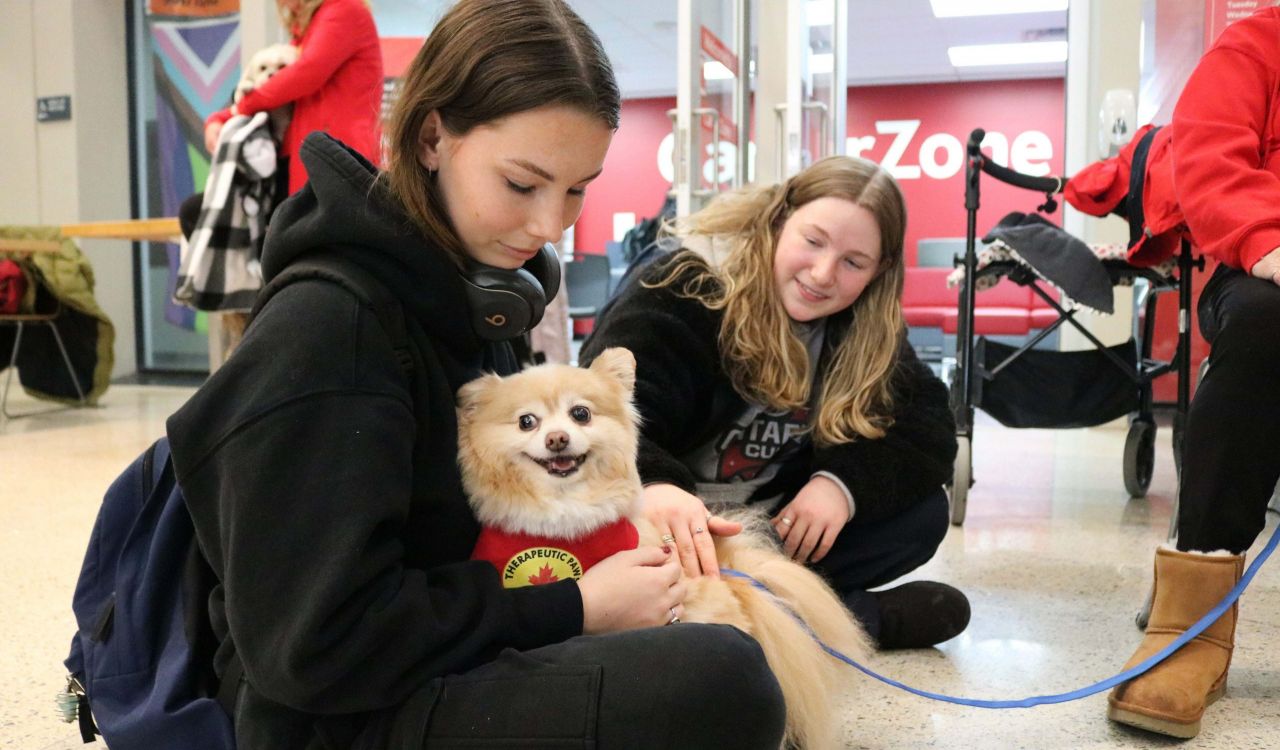 A small dog sits in a young woman’s lap while a second woman sits beside them.