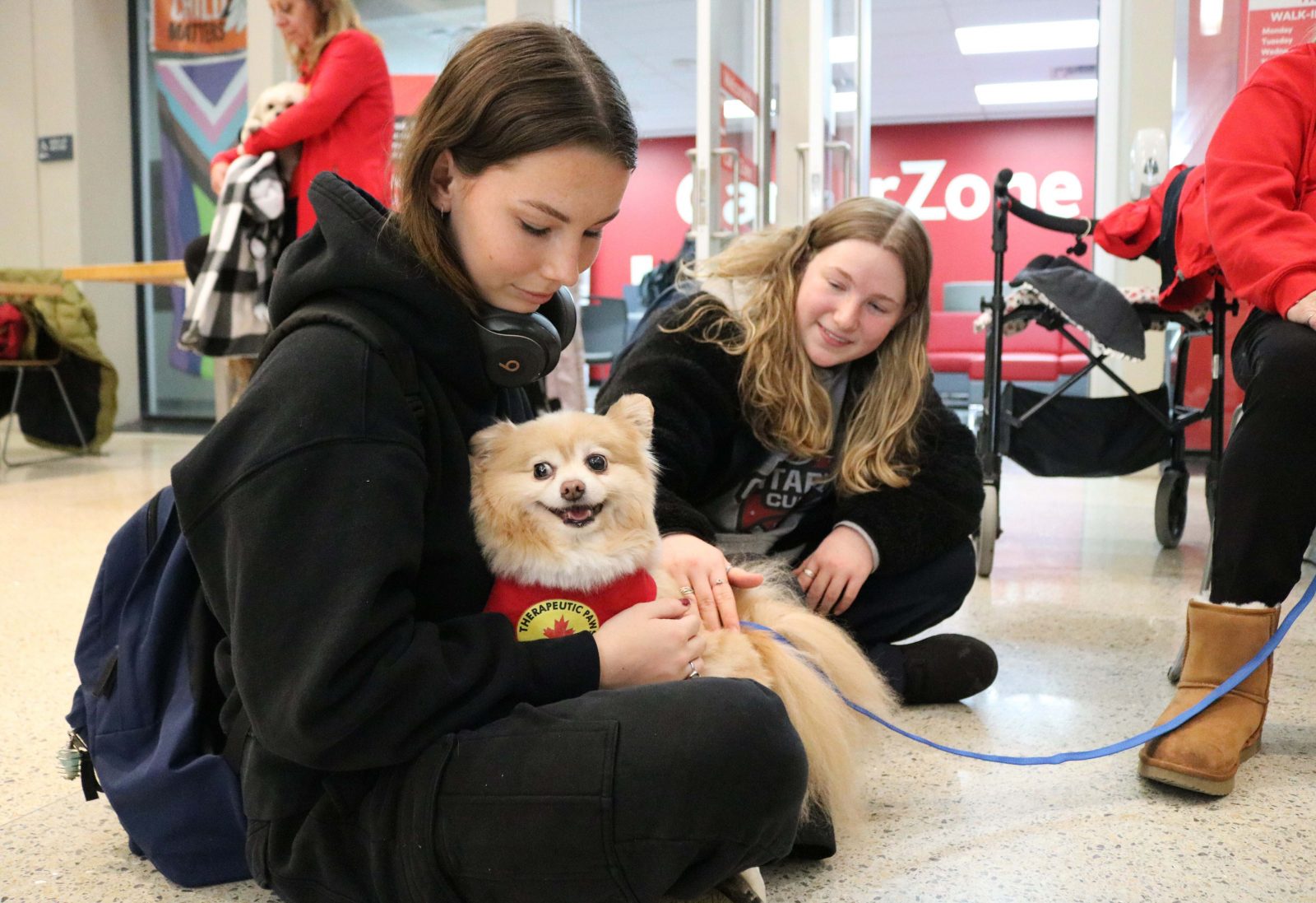 A small dog sits in a young woman’s lap while a second woman sits beside them.